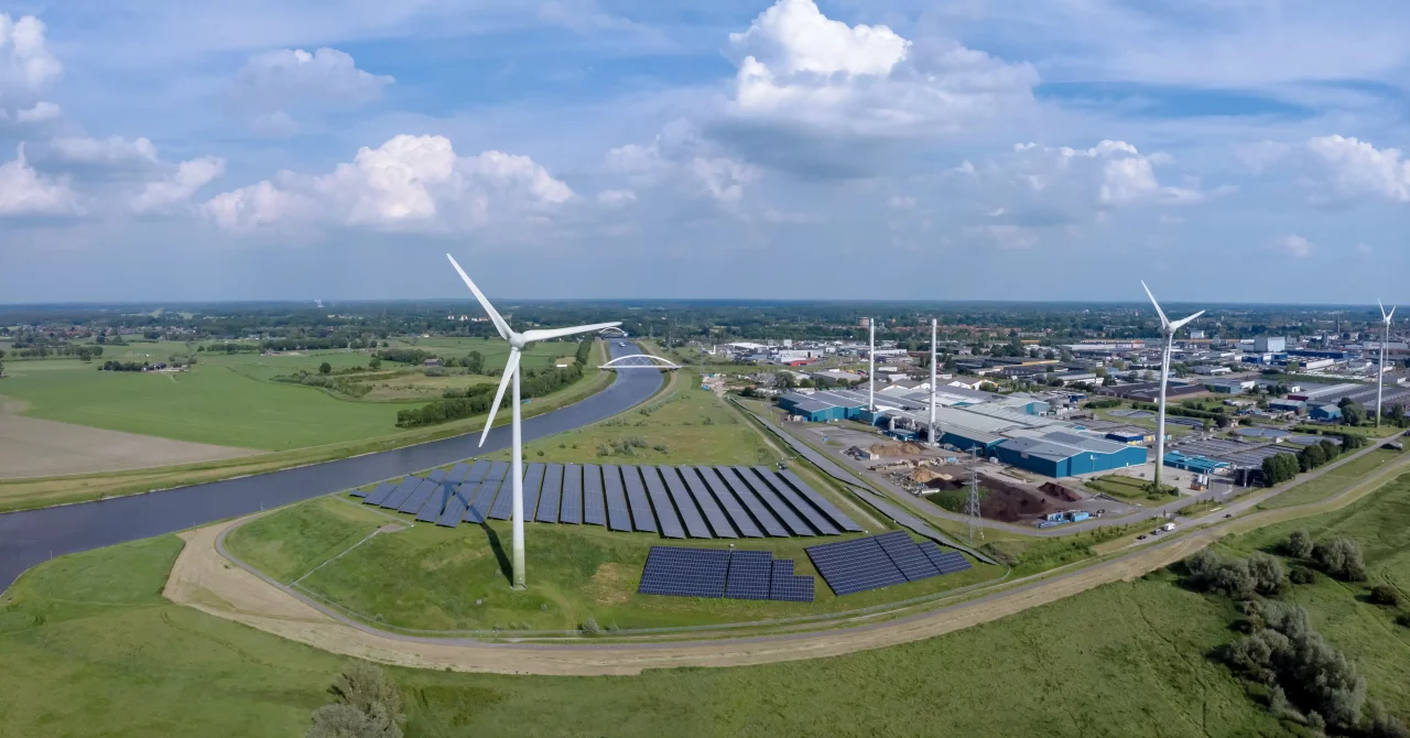 Industrial park next to a river in a grassy field with windmills and solar panels.