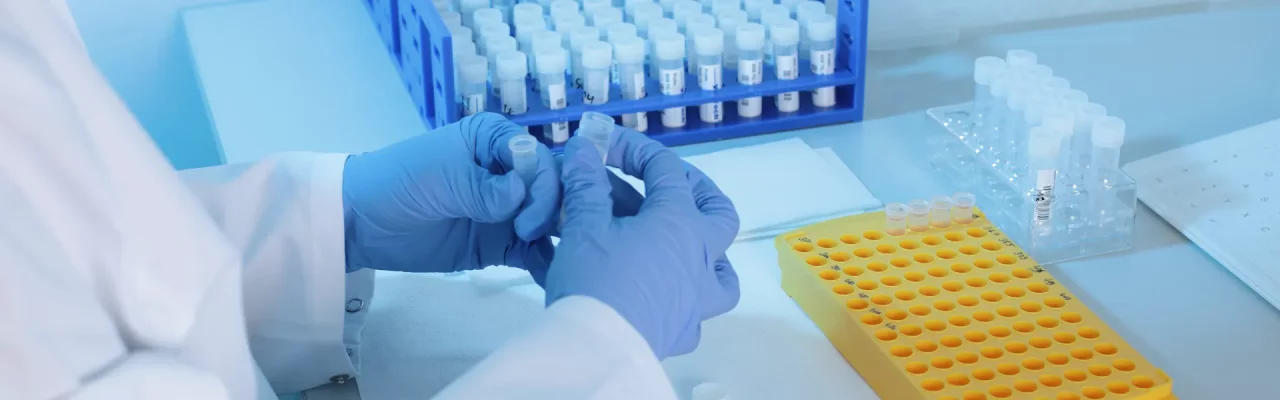 Handen met blauwe handschoenen en twee reageerbuisjes in het laboratorium van Valitech om te testen.